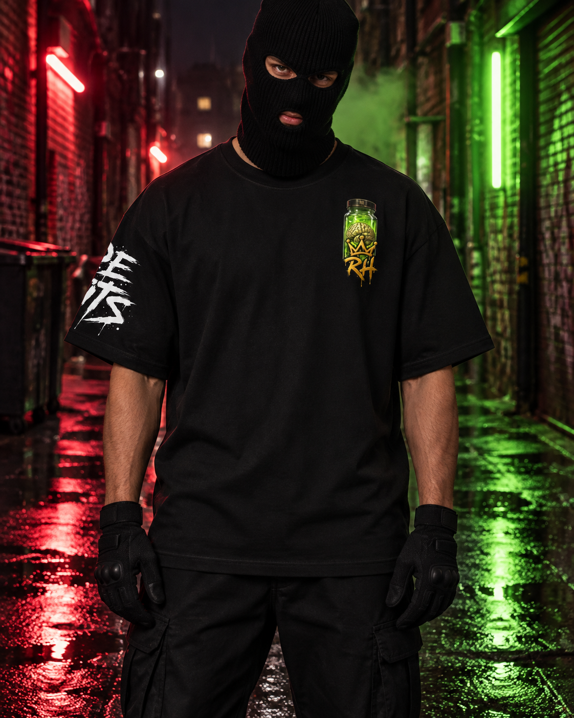 A person wearing a black balaclava, black t-shirt with a green and yellow chest graphic and white sleeve print, and black cargo pants stands in a wet alley at night with red and green neon lights reflecting on the ground.