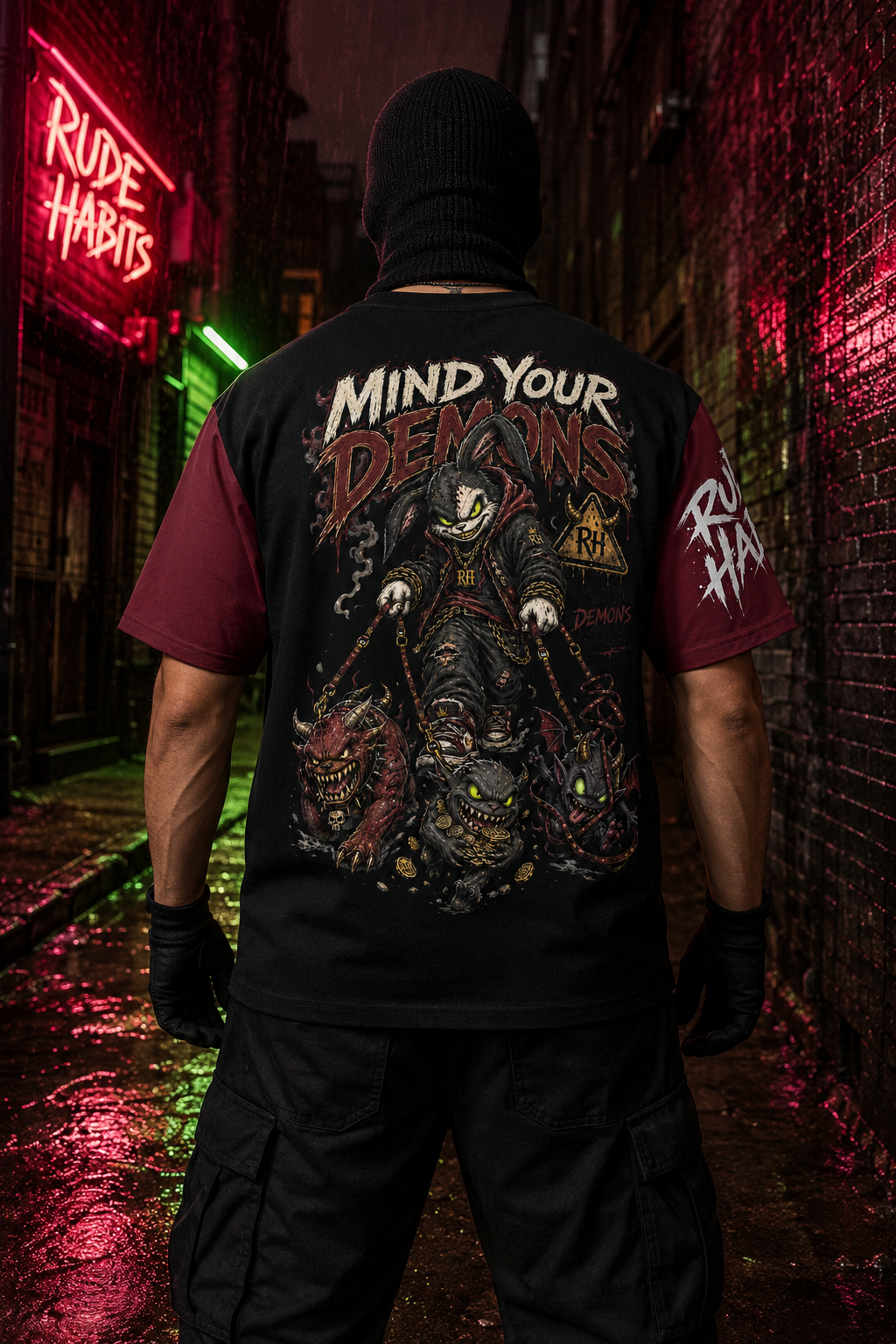 A person standing in a dark alley at night wearing a black graphic t-shirt with a large horror-themed back print reading 'Mind Your Demons' and 'Rude Habits' on the sleeve, photographed from behind.