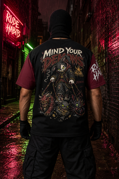 A person standing in a dark alley at night wearing a black graphic t-shirt with a large horror-themed back print reading 'Mind Your Demons' and 'Rude Habits' on the sleeve, photographed from behind.
