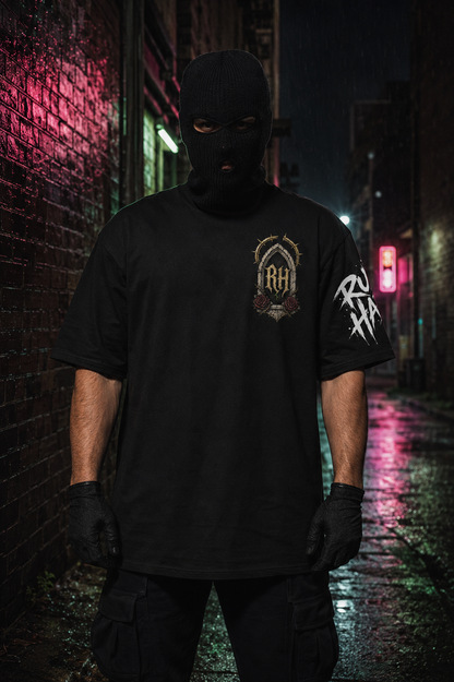 A person wearing a black balaclava mask, black gloves, and a black graphic t-shirt stands in a wet, neon-lit alleyway at night. The t-shirt features a gold and black crest-style graphic on the left chest and a white graphic on the right sleeve.