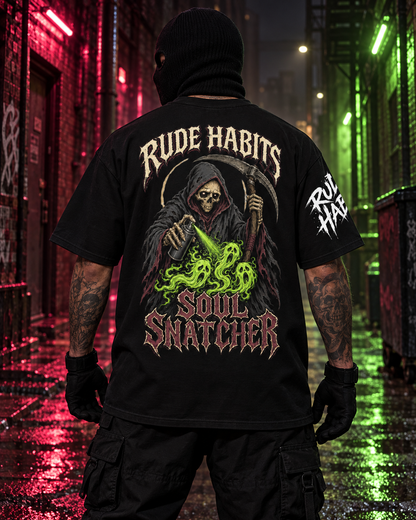 A person standing in a wet urban alley at night wearing a black graphic T-shirt shown from the back. The shirt features a grim reaper illustration with a skull, scythe, green snake-like energy, and the text 'RUDE HABITS SOUL SNATCHER' on the back, plus white text on the right sleeve.